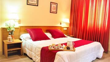 A hotel room with a bed, red curtains, a tray with breakfast items, and two wall-mounted lamps.
