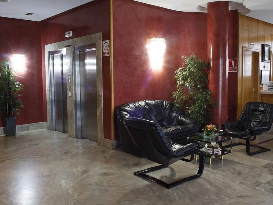 Een hal met een zwarte leren bank, twee stoelen, een salontafel, een potplant en een lift.