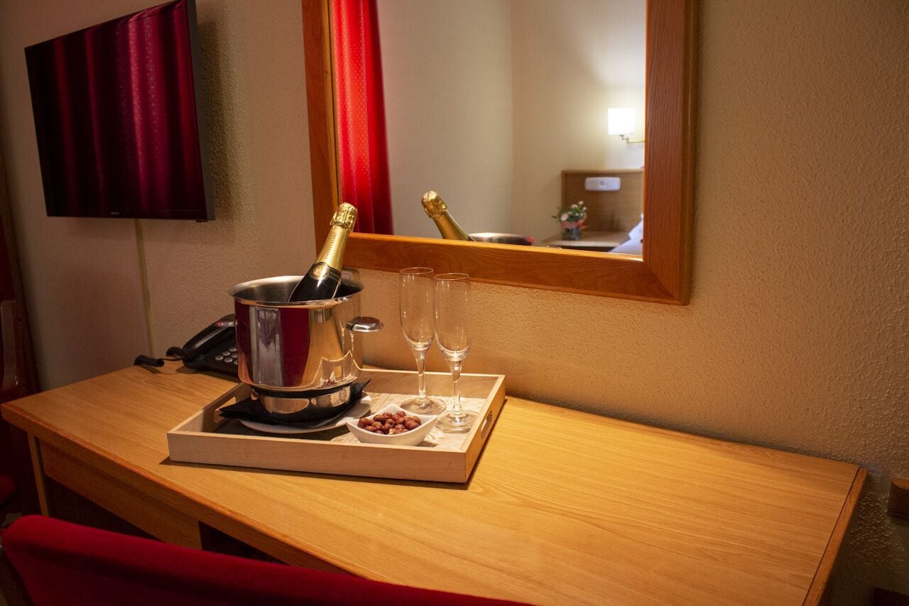 Habitación de hotel con un escritorio de madera, una botella de champán, dos copas y una bandeja con frutos secos.