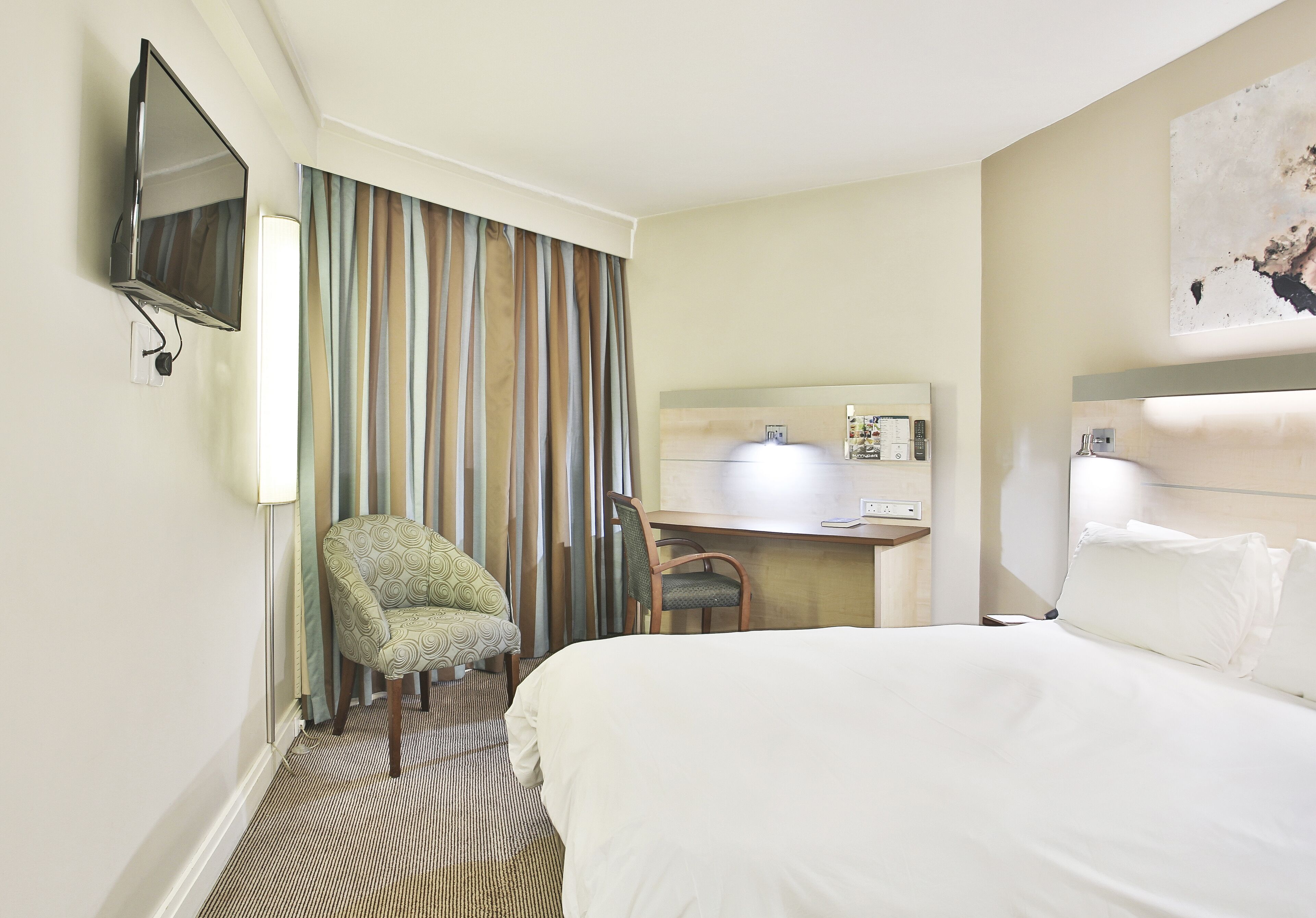 Una habitación de hotel con cama, escritorio, silla, televisión y baño.