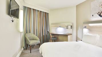 Una habitación de hotel con cama, escritorio, silla, televisión y baño.