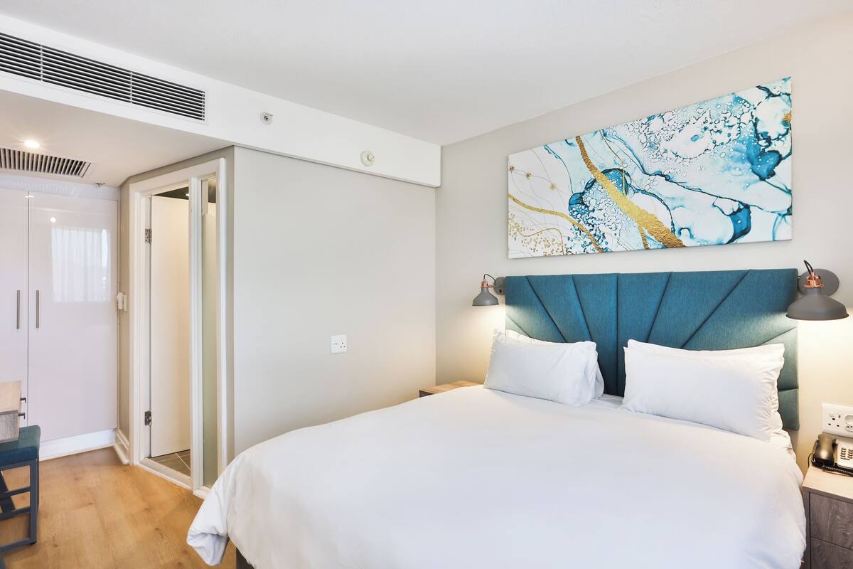 Un dormitorio con cama, una mesita de noche, una lámpara de pared y una puerta que da a un baño.
