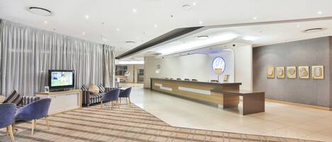 A modern hotel lobby with a reception desk, seating area, and a television.