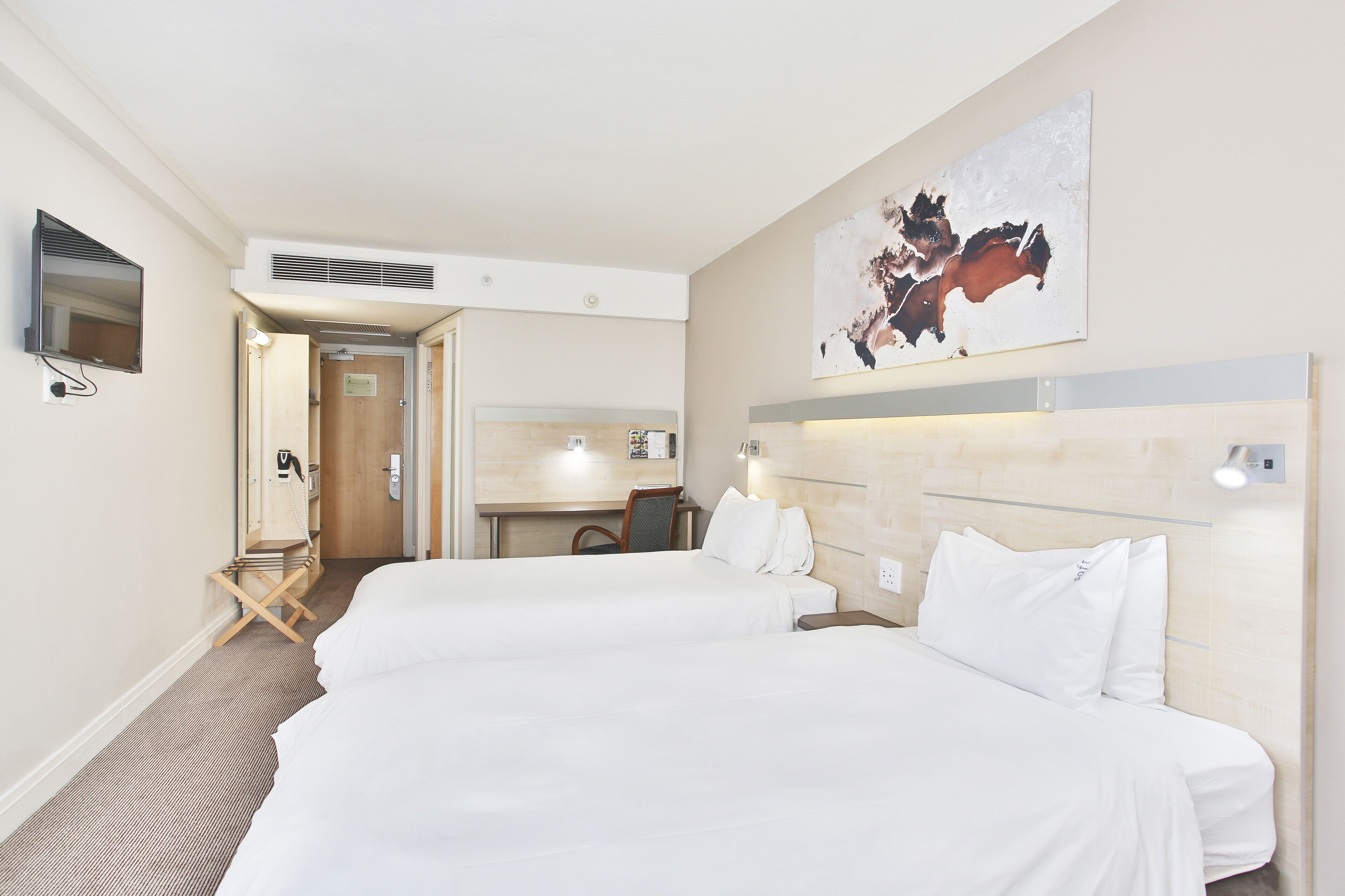 A hotel room with two beds, a desk, and a bathroom.