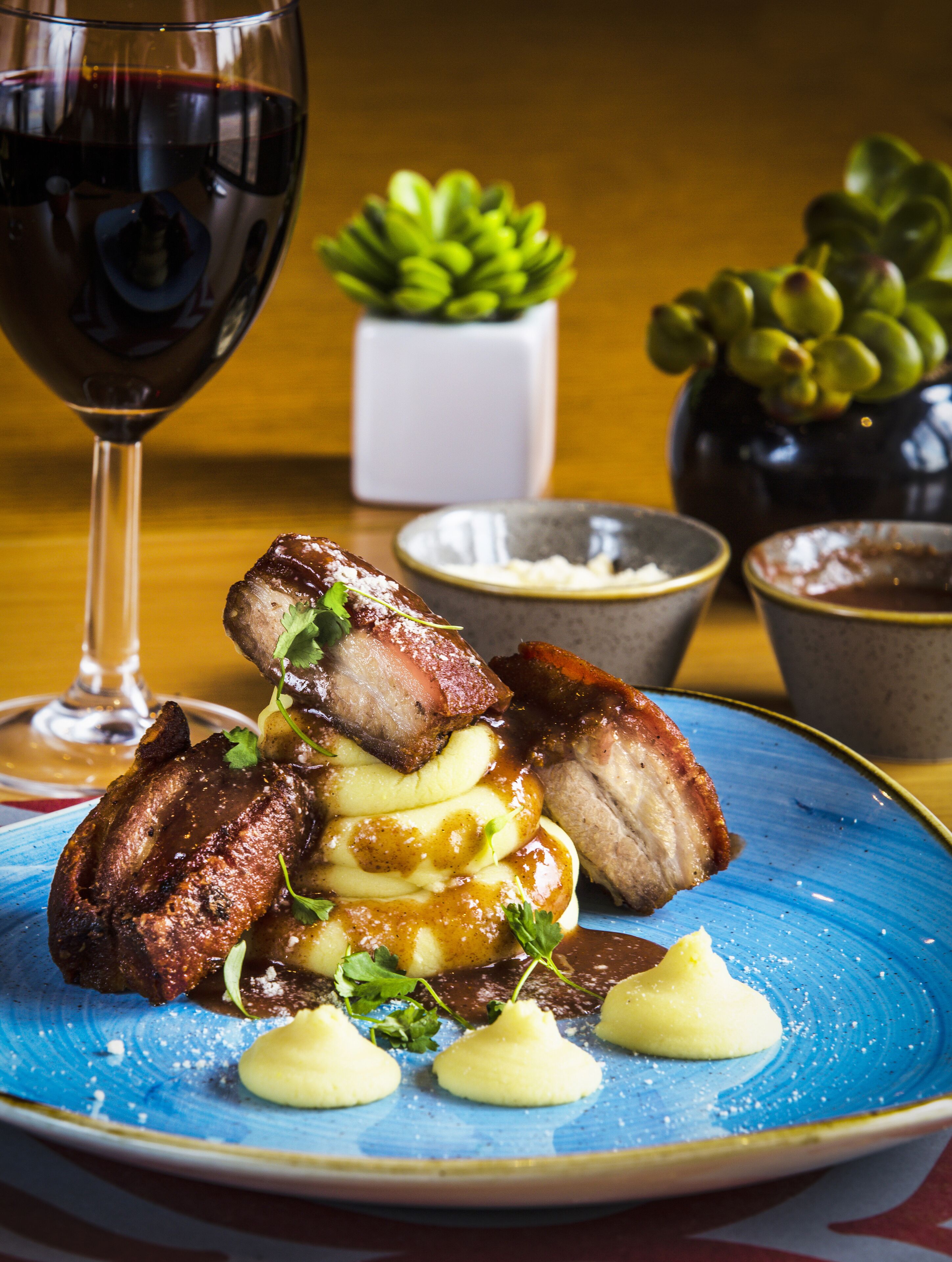 A plate of food with meat, potatoes, and a glass of red wine.