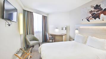 A hotel room with a large bed, a desk, a chair, a TV, and a painting on the wall.