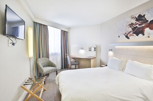 Quarto de hotel com uma cama grande, uma escrivaninha, uma cadeira, uma televisão e um quadro na parede.