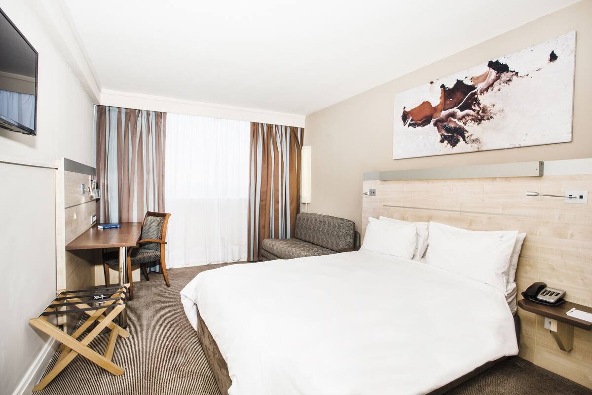 Habitación de hotel con una cama grande, un escritorio con una silla, un teléfono y un cuadro en la pared.