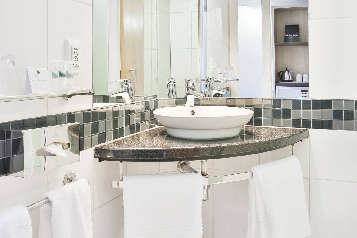 Un baño moderno con un espejo grande, azulejos blancos y encimera de granito.