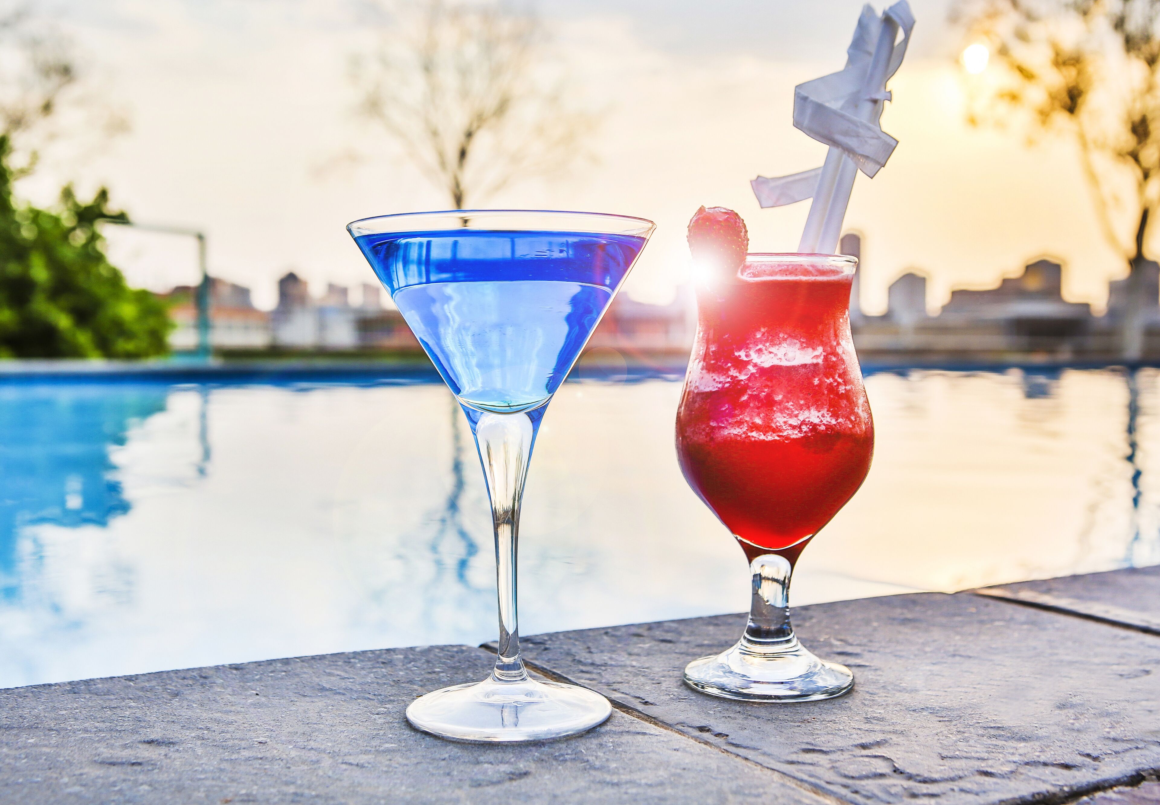 Two drinks, one blue and one red, on a table by a pool.