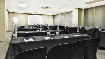 A conference room with multiple tables, chairs, water bottles, and a projector screen.