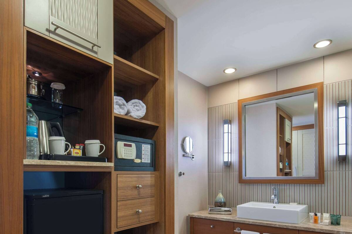 Een moderne badkamer met een houten wastafelmeubel, een grote spiegel en een ingebouwde koelkast.