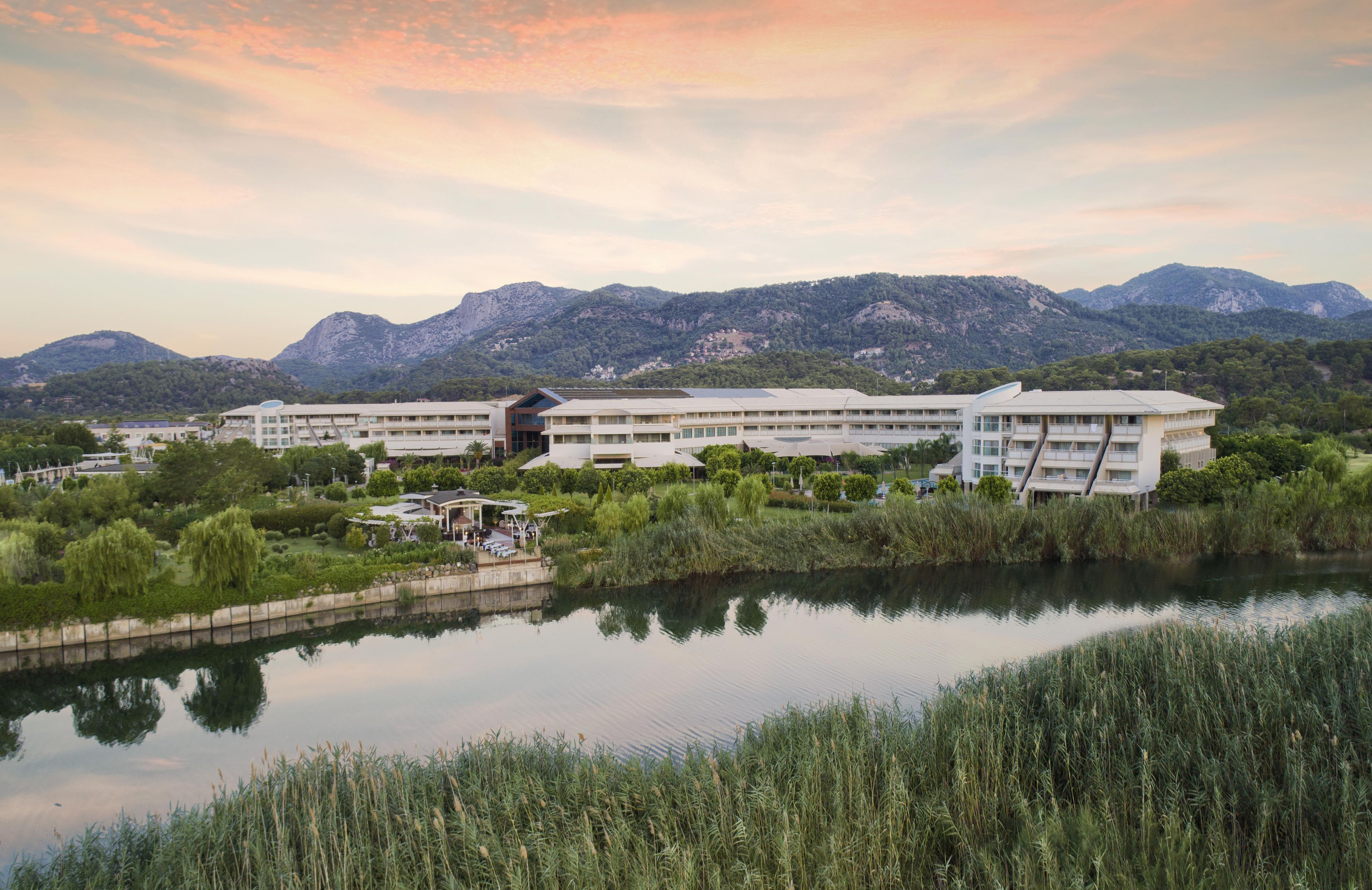 A hotel with multiple floors, a swimming pool, and a view of mountains in the background.