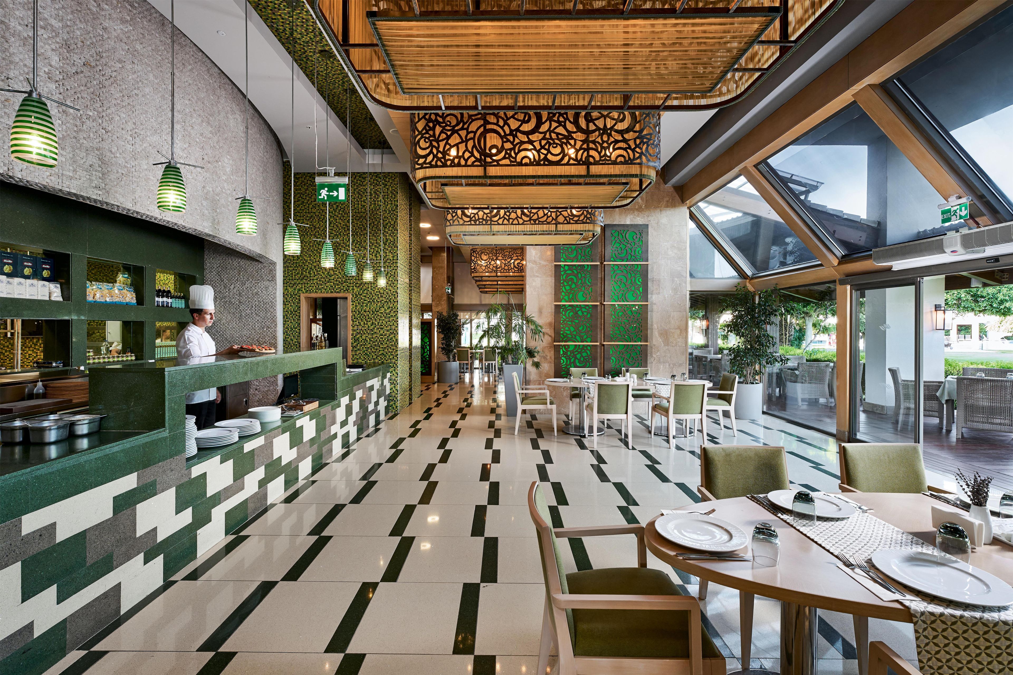 Interior de restaurante con un chef preparando comida, una recepción y un comedor con mesas y sillas.