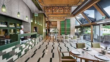 Interior de restaurante con un chef preparando comida, una recepción y un comedor con mesas y sillas.