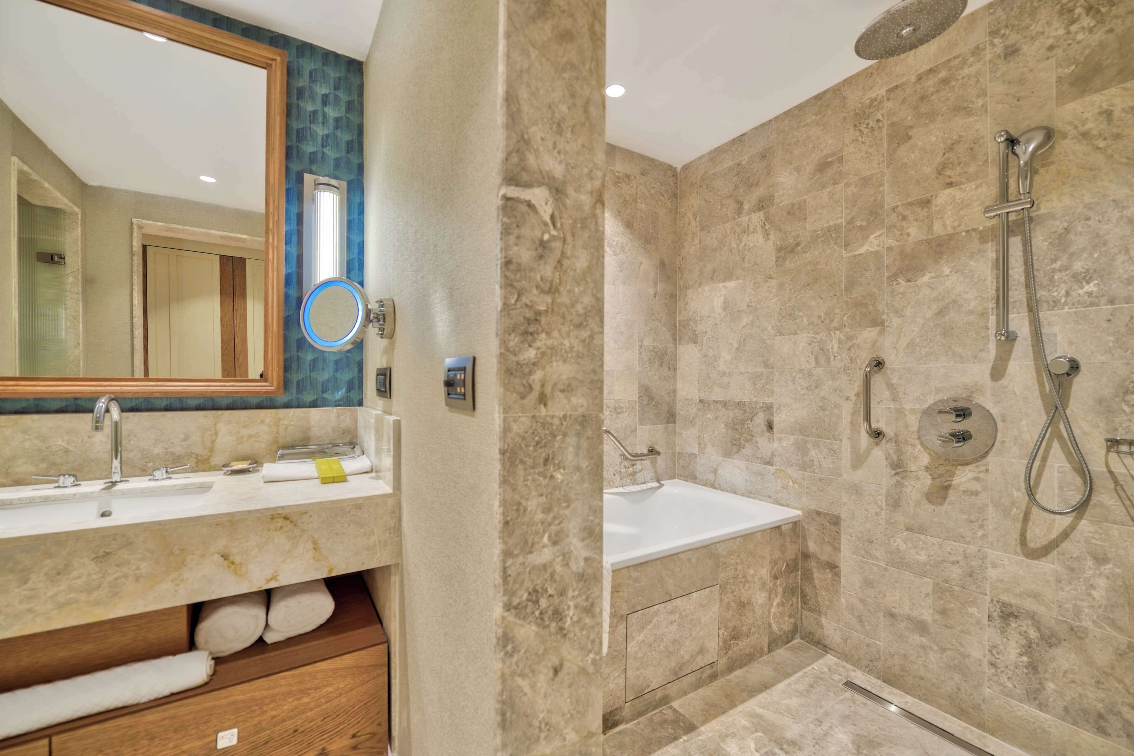 A modern bathroom with a marble shower, a sink, and a mirror.