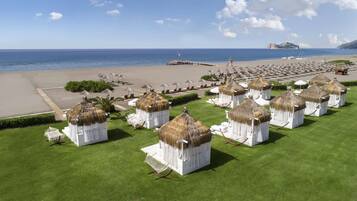 A beachside resort with thatched-roof huts, sun loungers, and a pier extending into the sea.