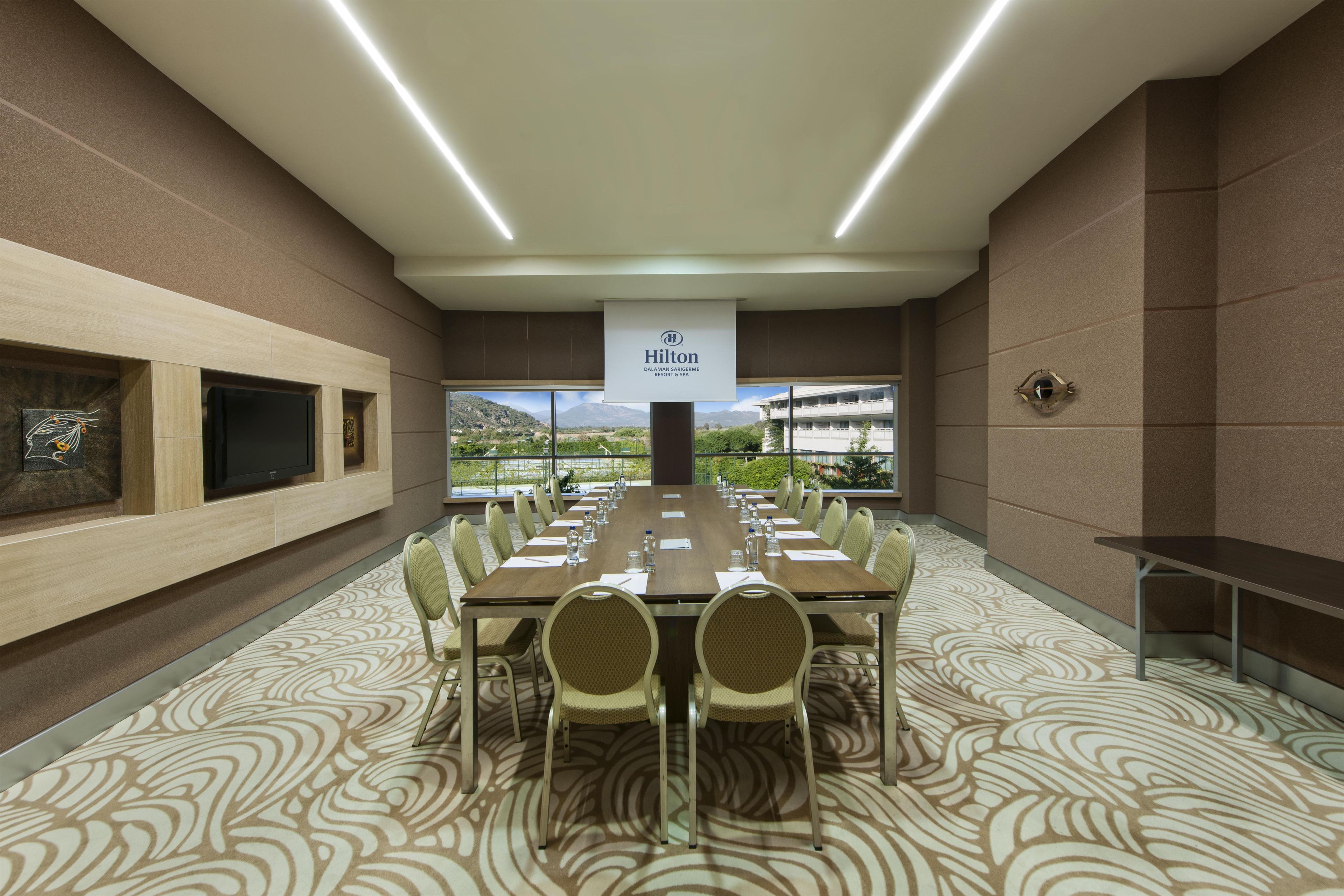 Un salón de conferencias con una mesa larga, sillas y un cartel.