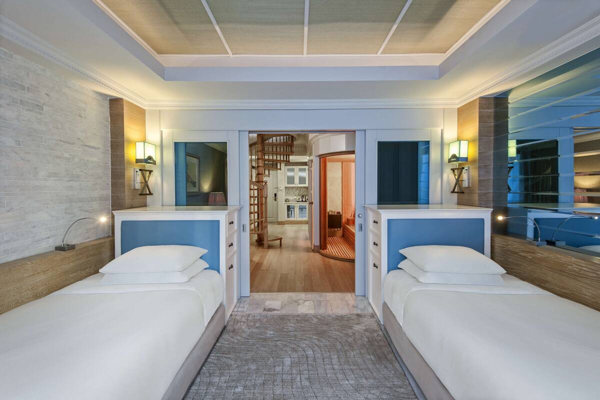 Een hotelkamer met twee bedden, een houten vloer, een wenteltrap en uitzicht op de keuken.