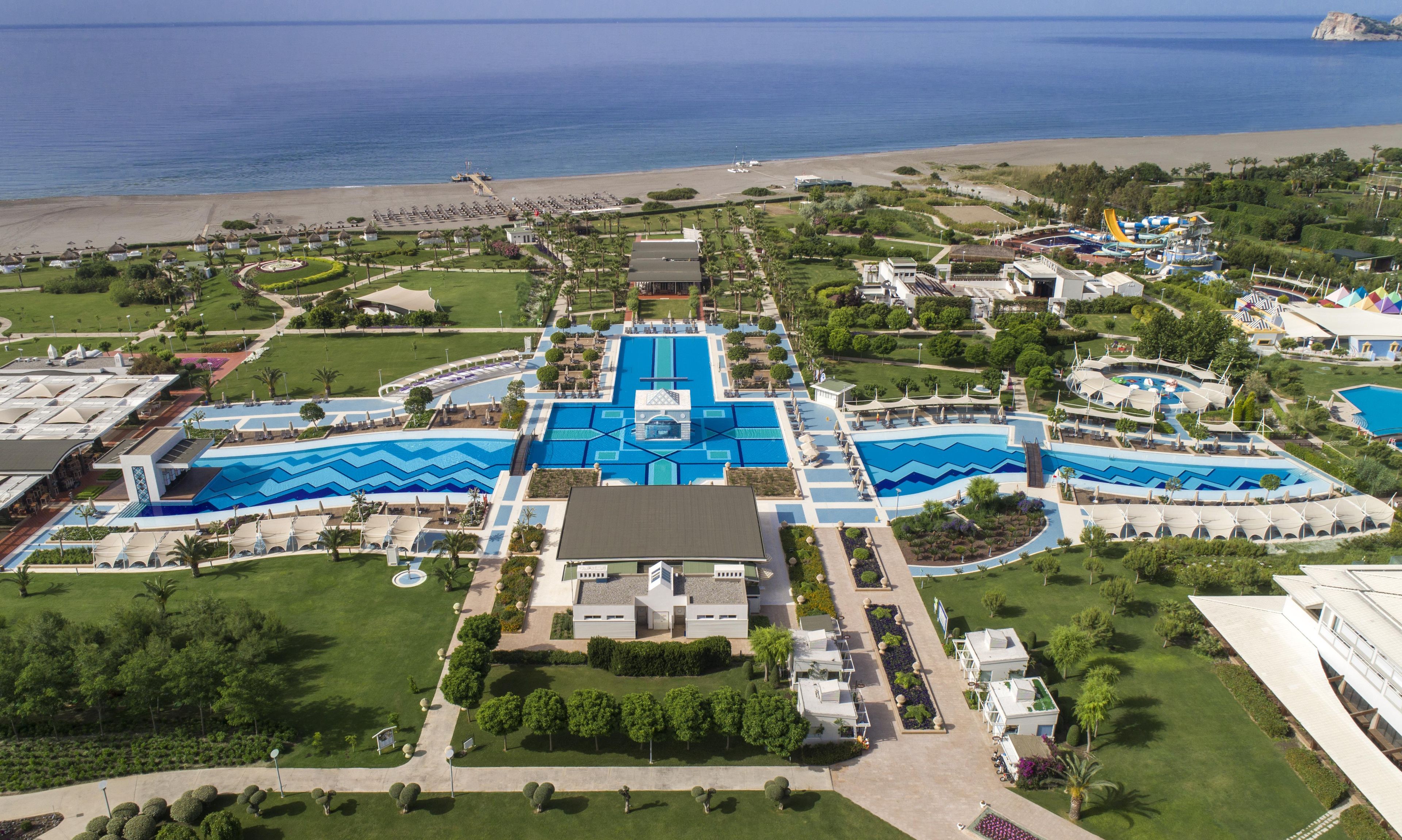 Un resort con múltiples piscinas, una playa y un edificio grande en el centro.