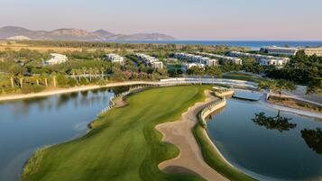 A golf course with a water hazard, surrounded by residential buildings and a mountain range in the background.