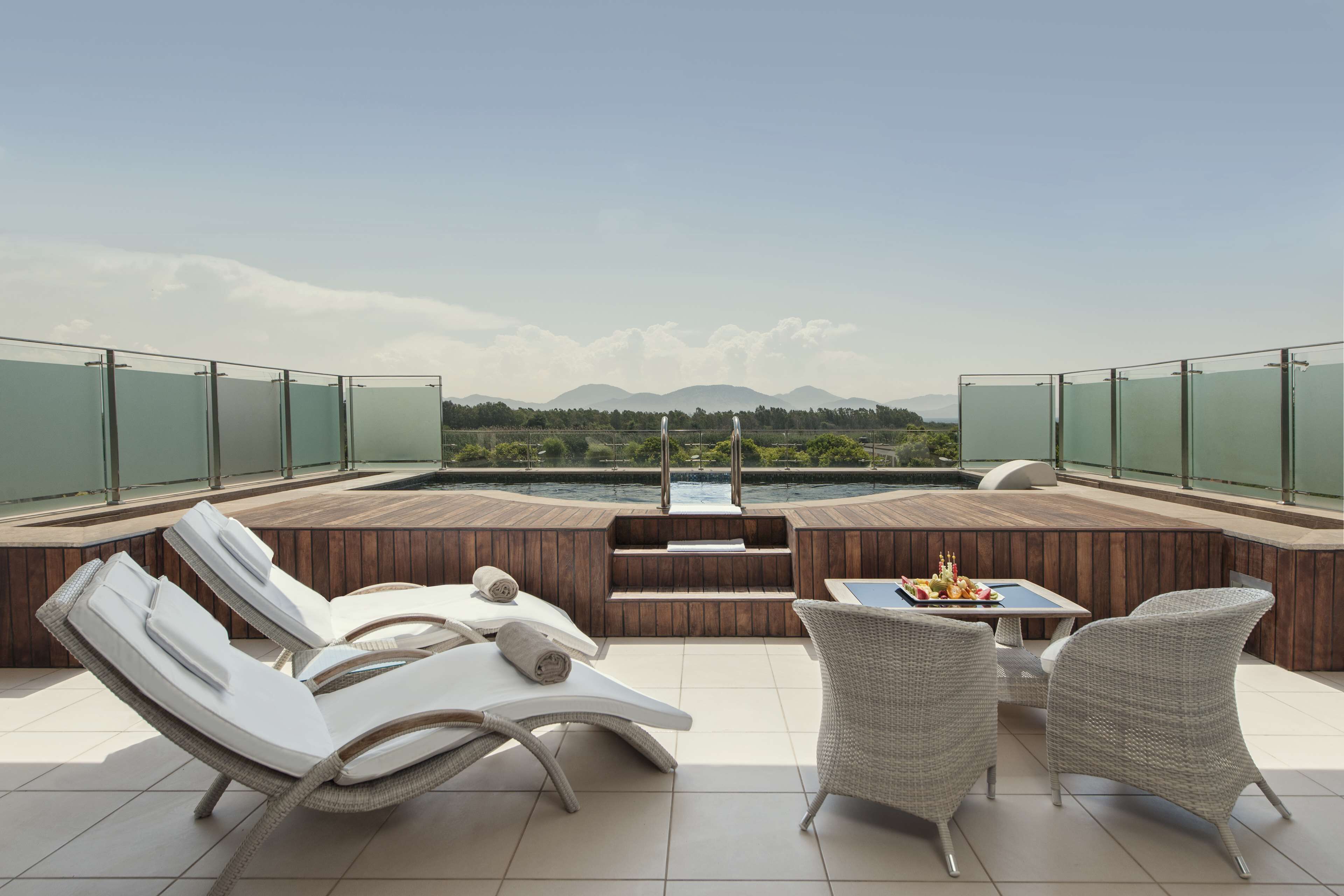 A rooftop terrace with lounge chairs, a table, and a view of a body of water and mountains.
