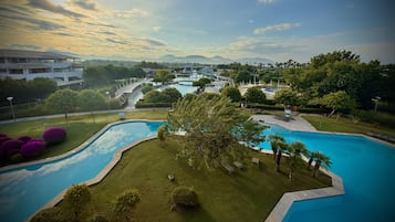 A resort with a large swimming pool, lush greenery, and a view of distant mountains.