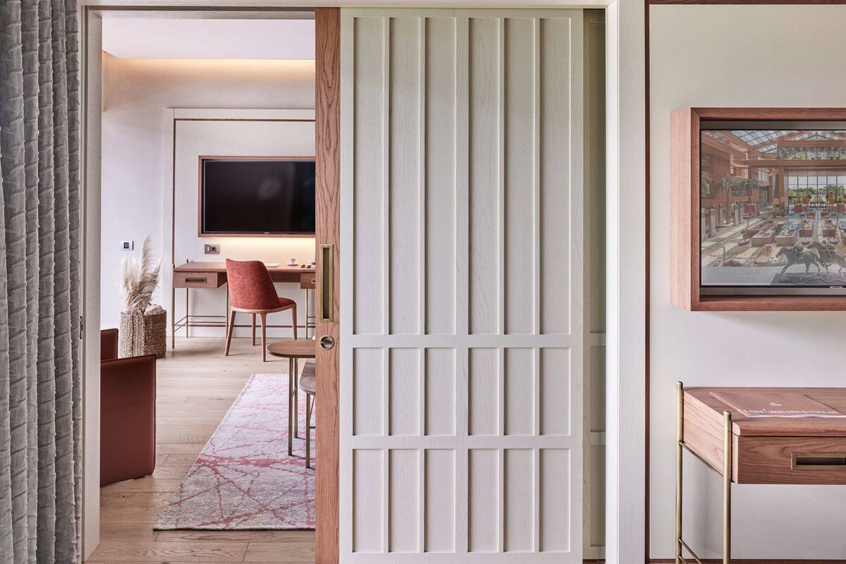 Ein modernes Hotelzimmer mit Holzboden, Schreibtisch mit Computer, Fernseher und großem Fenster.