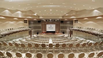 A conference room with a stage, seating arranged in a semi-circular pattern, and a large screen displaying the Hilton logo.
