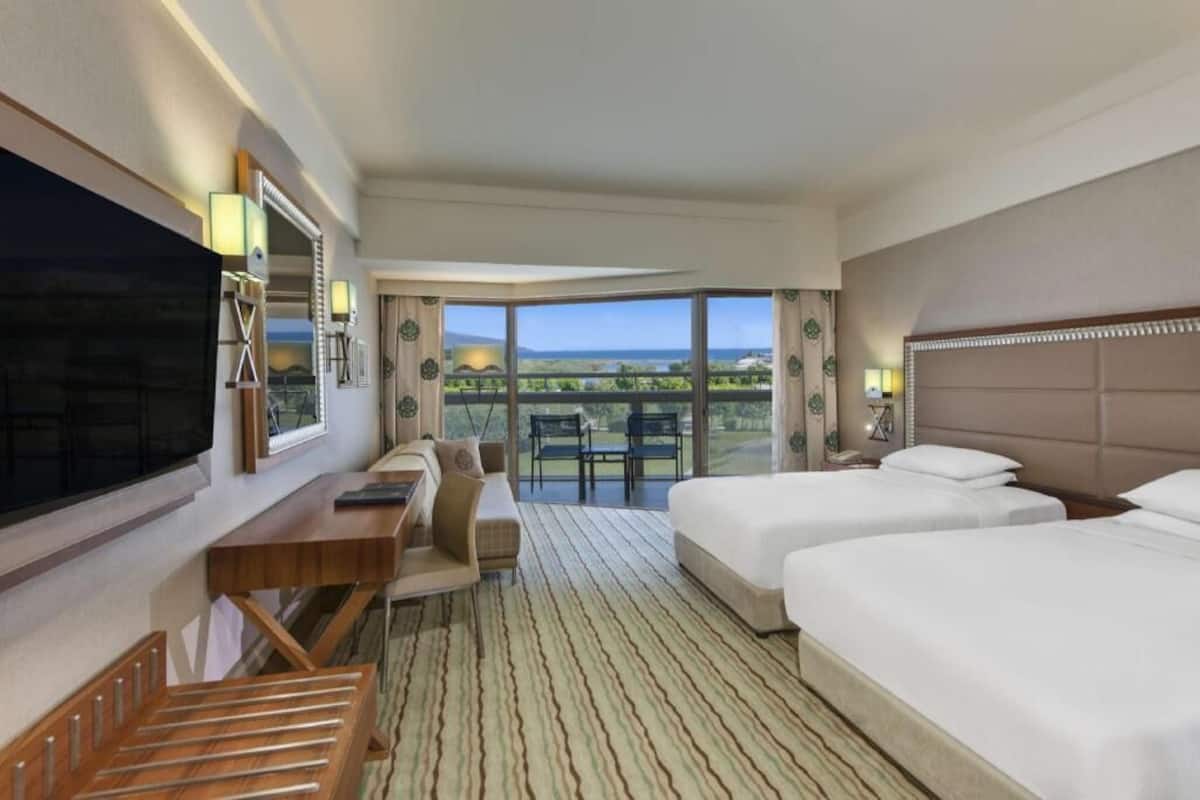 Ein Hotelzimmer mit großem Fernseher, Schreibtisch, zwei Betten und Blick auf die Landschaft.