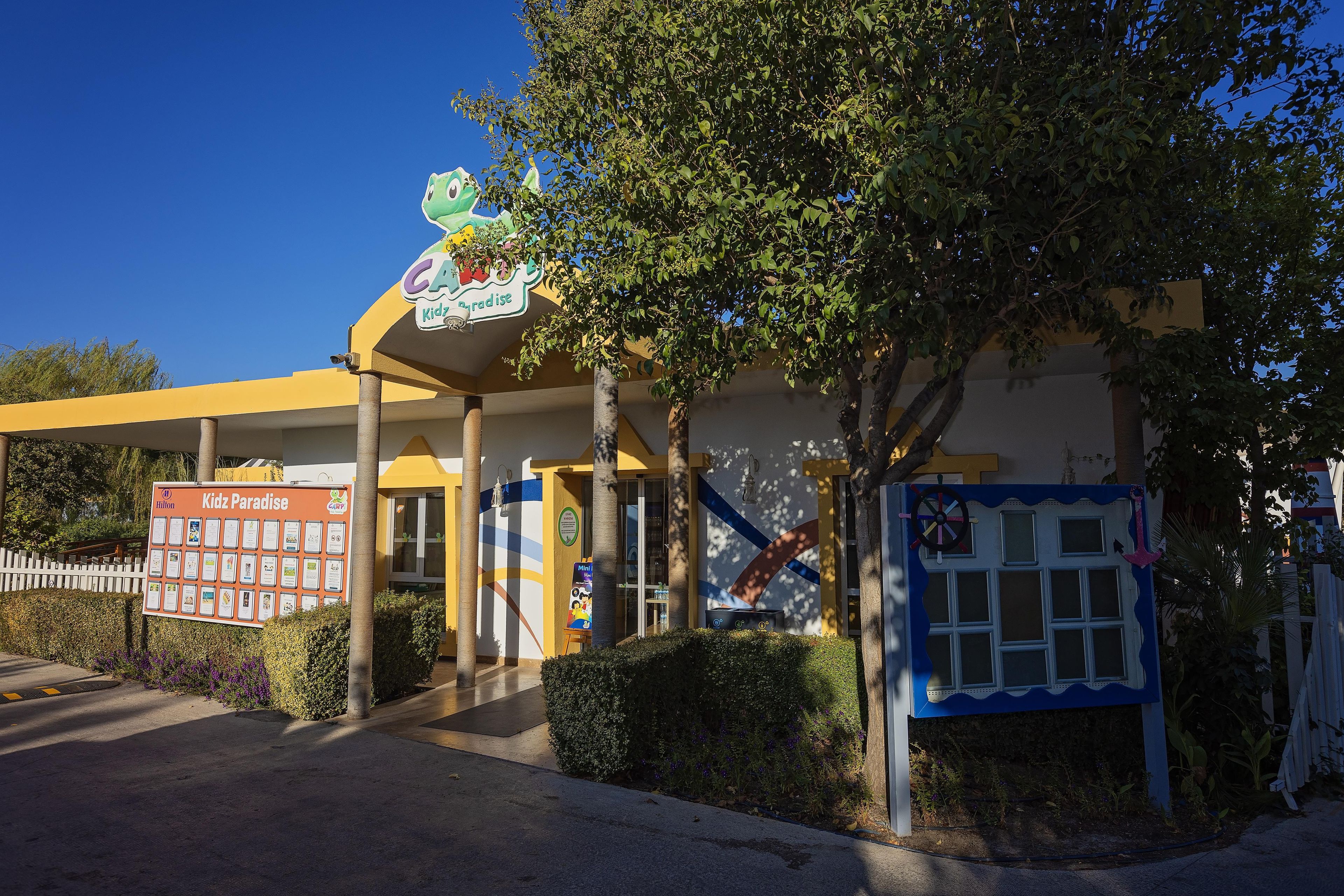 A building with a sign for Kidz Paradise, a children's play area, and a Hilton hotel sign.