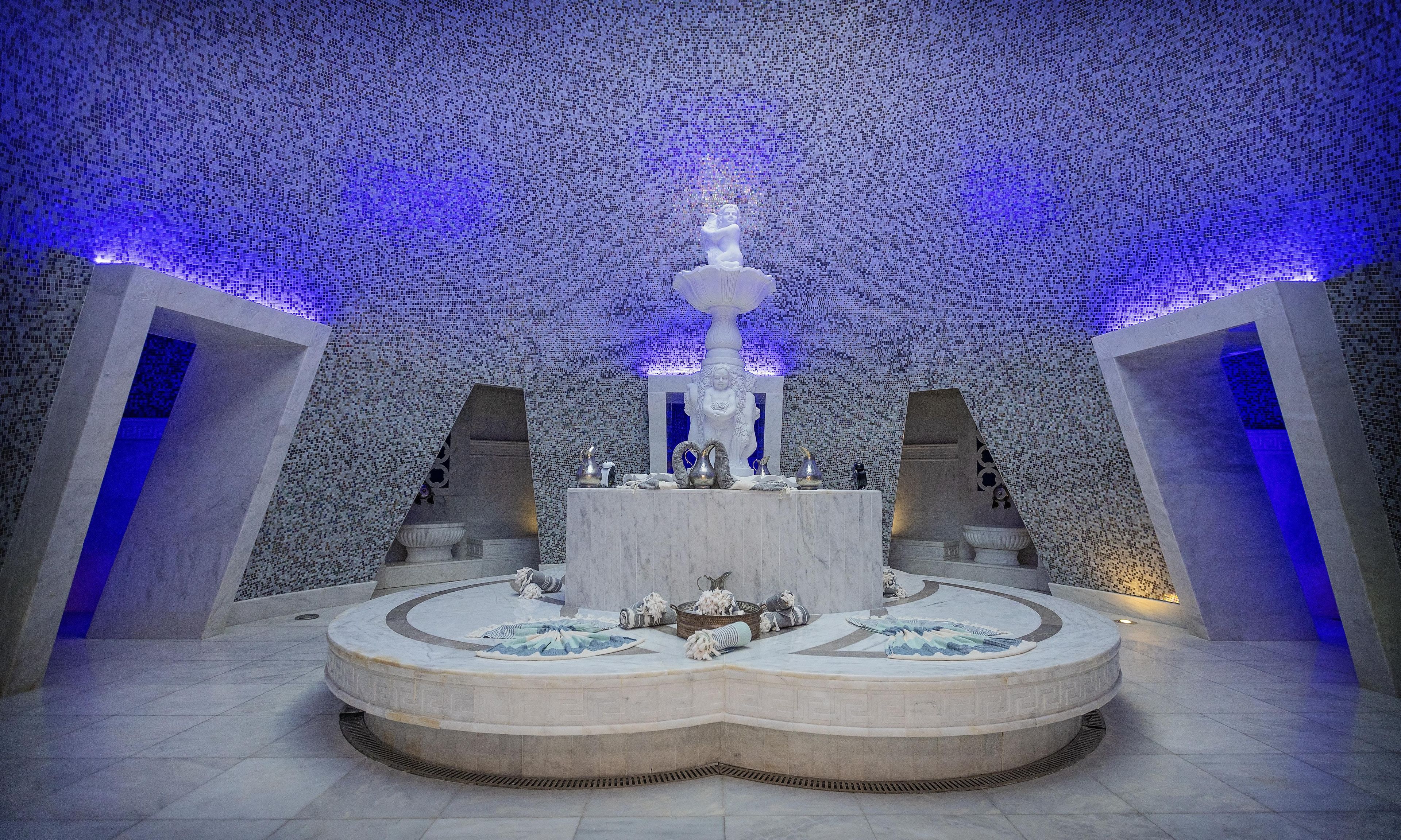 A circular marble fountain with a statue in the center, surrounded by a tiled floor and walls.