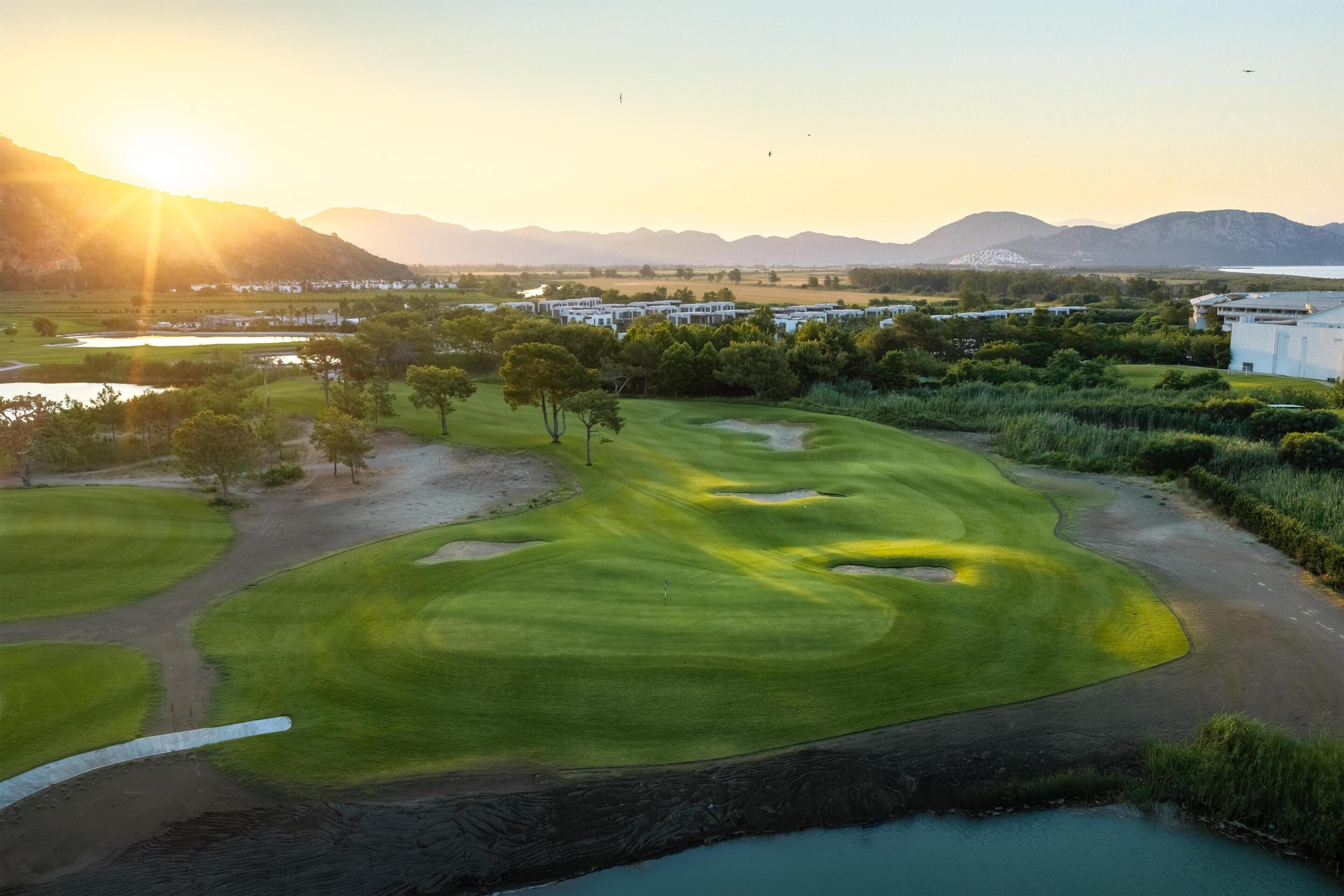 Ein Golfplatz mit einem Wasserschutzgebiet, Bäumen und Gebäuden im Hintergrund.