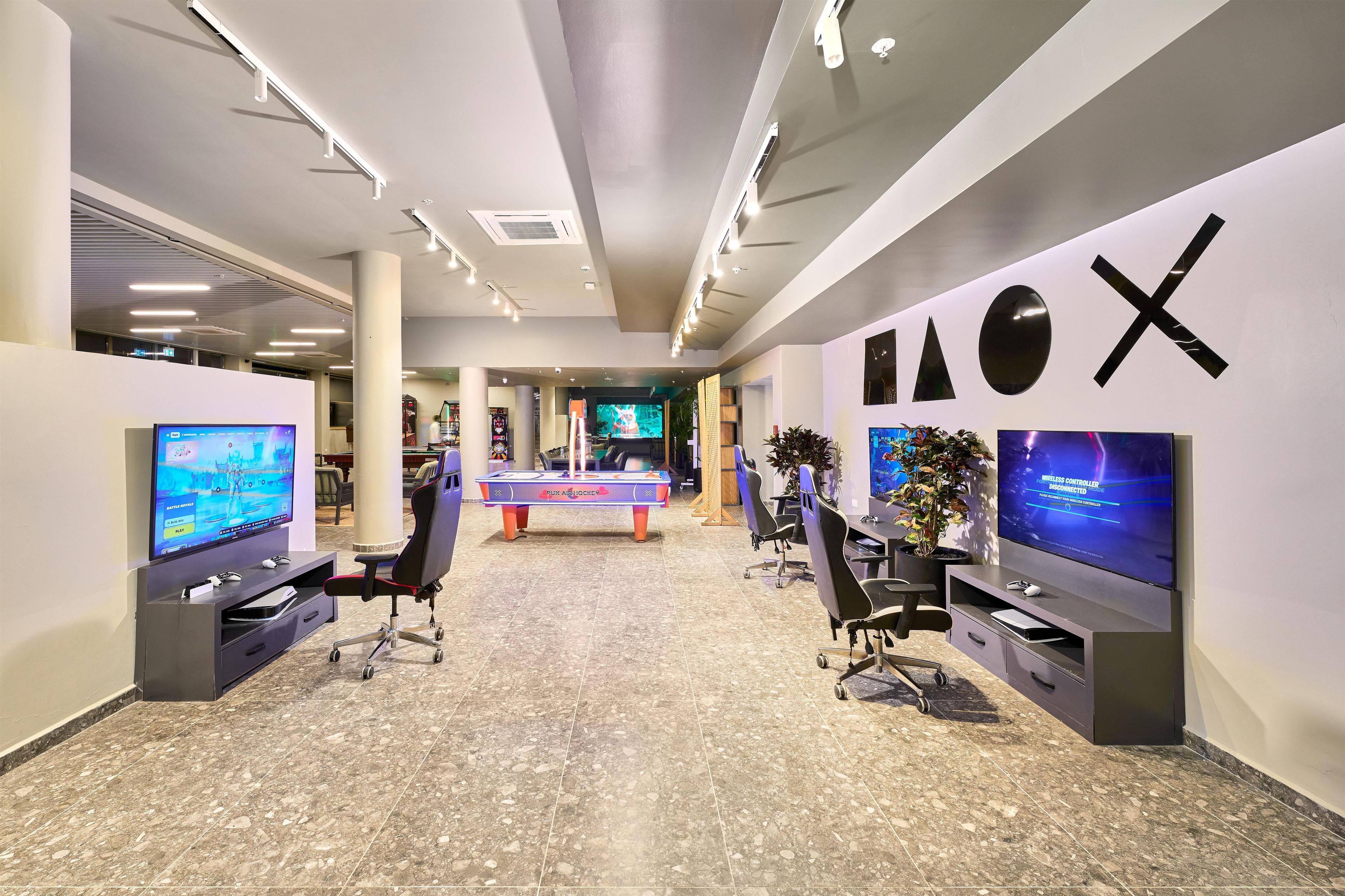 A modern gaming lounge with multiple gaming stations, including a foosball table, and large flat-screen TVs.