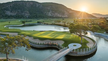 Un campo de golf con un puente sobre el agua, rodeado de colinas.