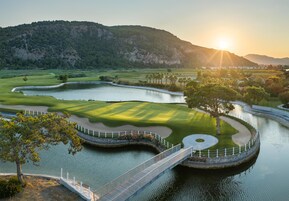 Un campo de golf con un puente sobre el agua, rodeado de colinas.