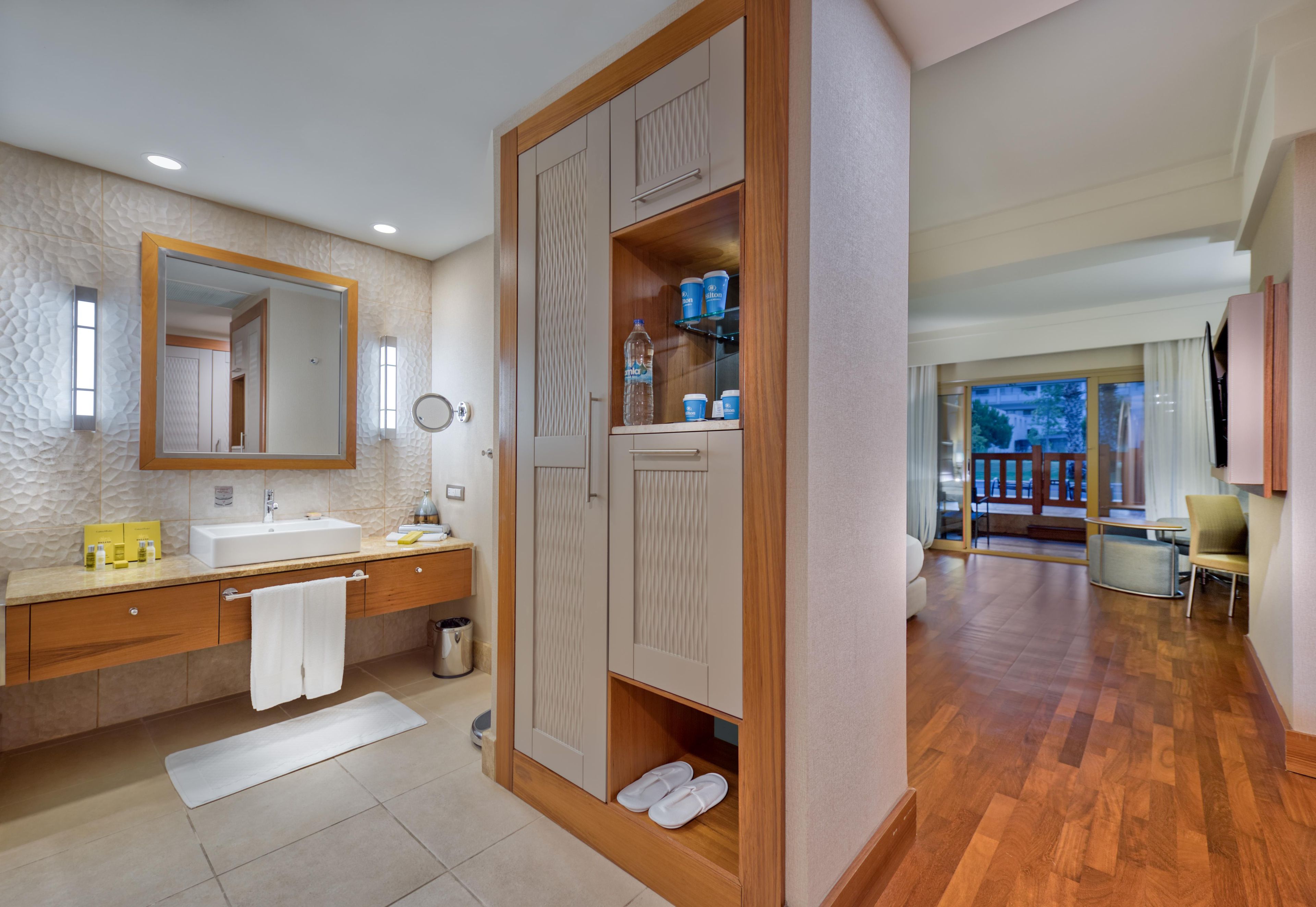 Un baño moderno con un espejo grande, un lavamanos y tocador. Hay un armario de madera con un espejo arriba y un estante con artículos de aseo.