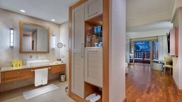Un baño moderno con un espejo grande, un lavamanos y tocador. Hay un armario de madera con un espejo arriba y un estante con artículos de aseo.