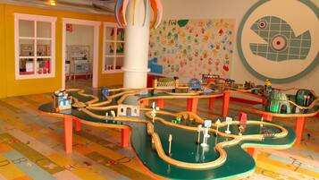 Zona infantil con suelo tipo laberinto, estructuras de juego coloridas y una pared con huellas de manos.