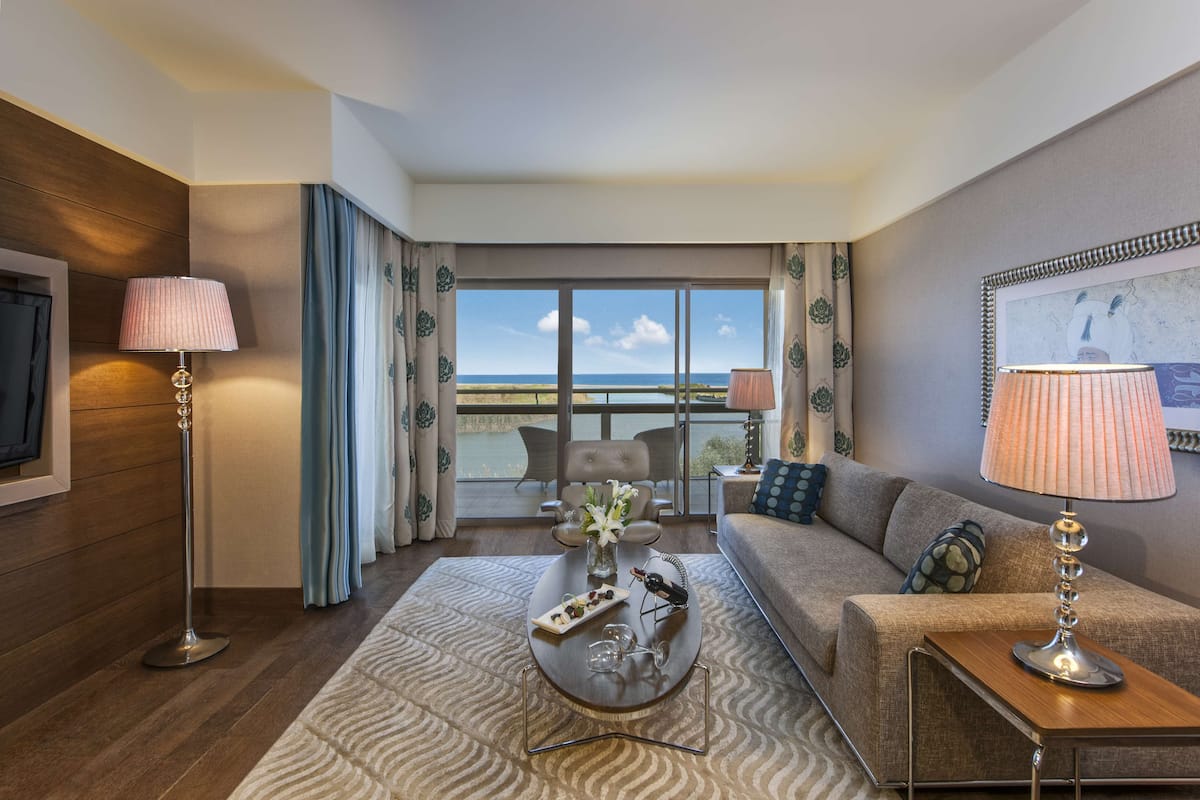 Een hotelkamer met een balkon, een bank, een bijzettafeltje met decoratieve objecten en een televisie aan de linker muur.