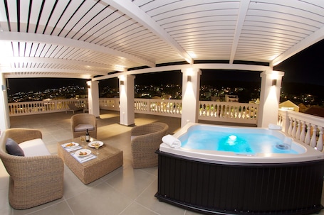 A hot tub area with wicker furniture and a view of the city at night.