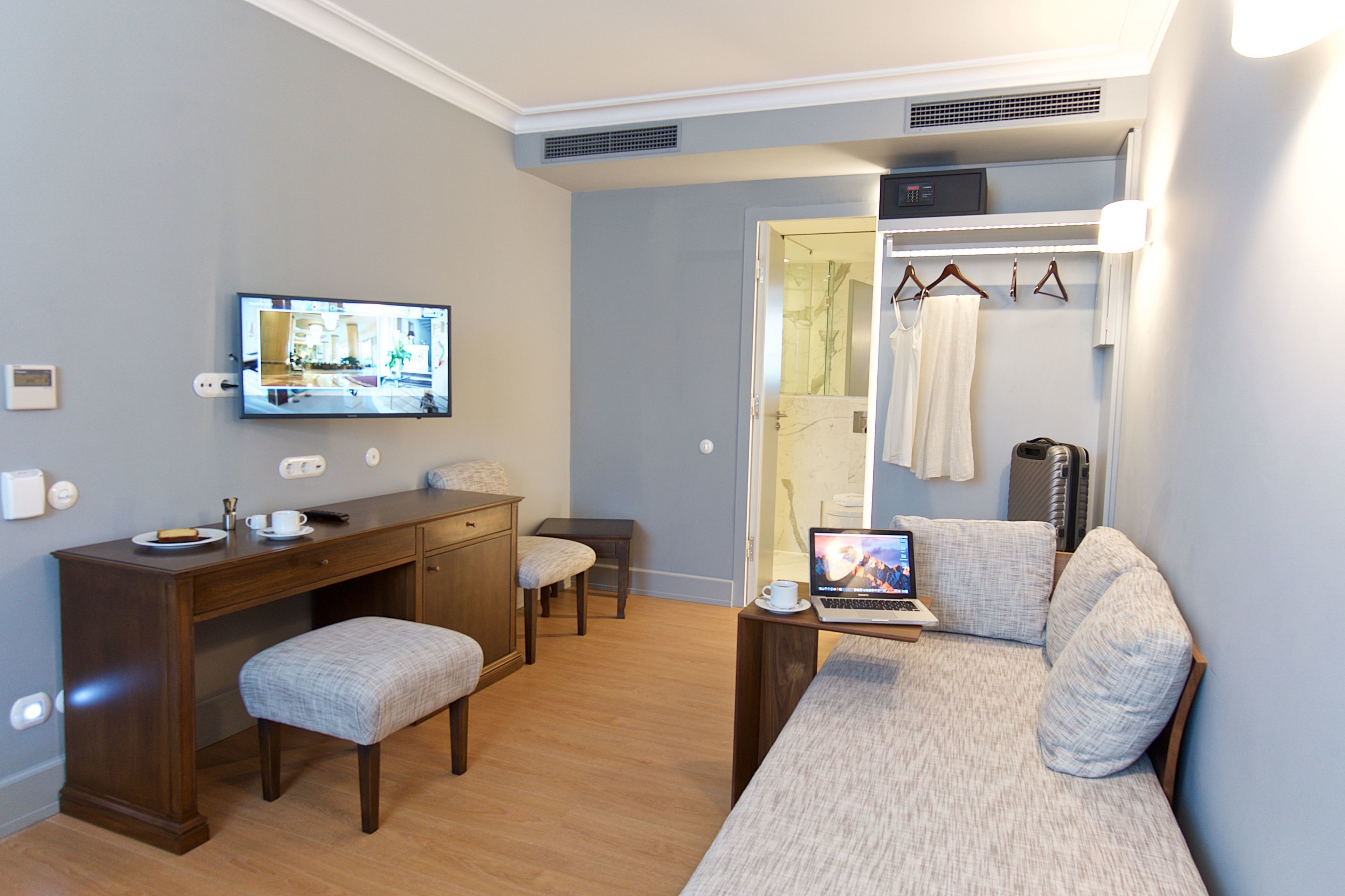 Una habitación de hotel compacta con un escritorio de madera, un sofá cómodo, un televisor y una computadora portátil.