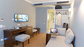 Una habitación de hotel compacta con un escritorio de madera, un sofá cómodo, un televisor y una computadora portátil.