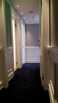 Un couloir avec des portes blanches, une moquette sombre et des luminaires encastrés.