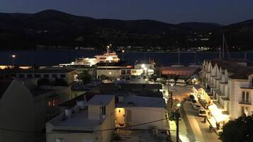 Un pueblo costero de noche con un barco grande amarrado en el puerto, edificios a lo largo del malecón y una carretera que lleva al puerto.