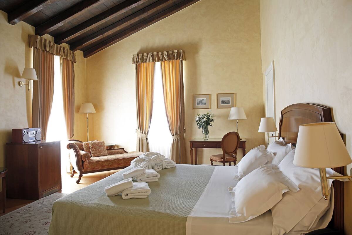 Una camera d'hotel con un letto grande, una testiera in legno, una scrivania con una sedia, un divano e una radio.