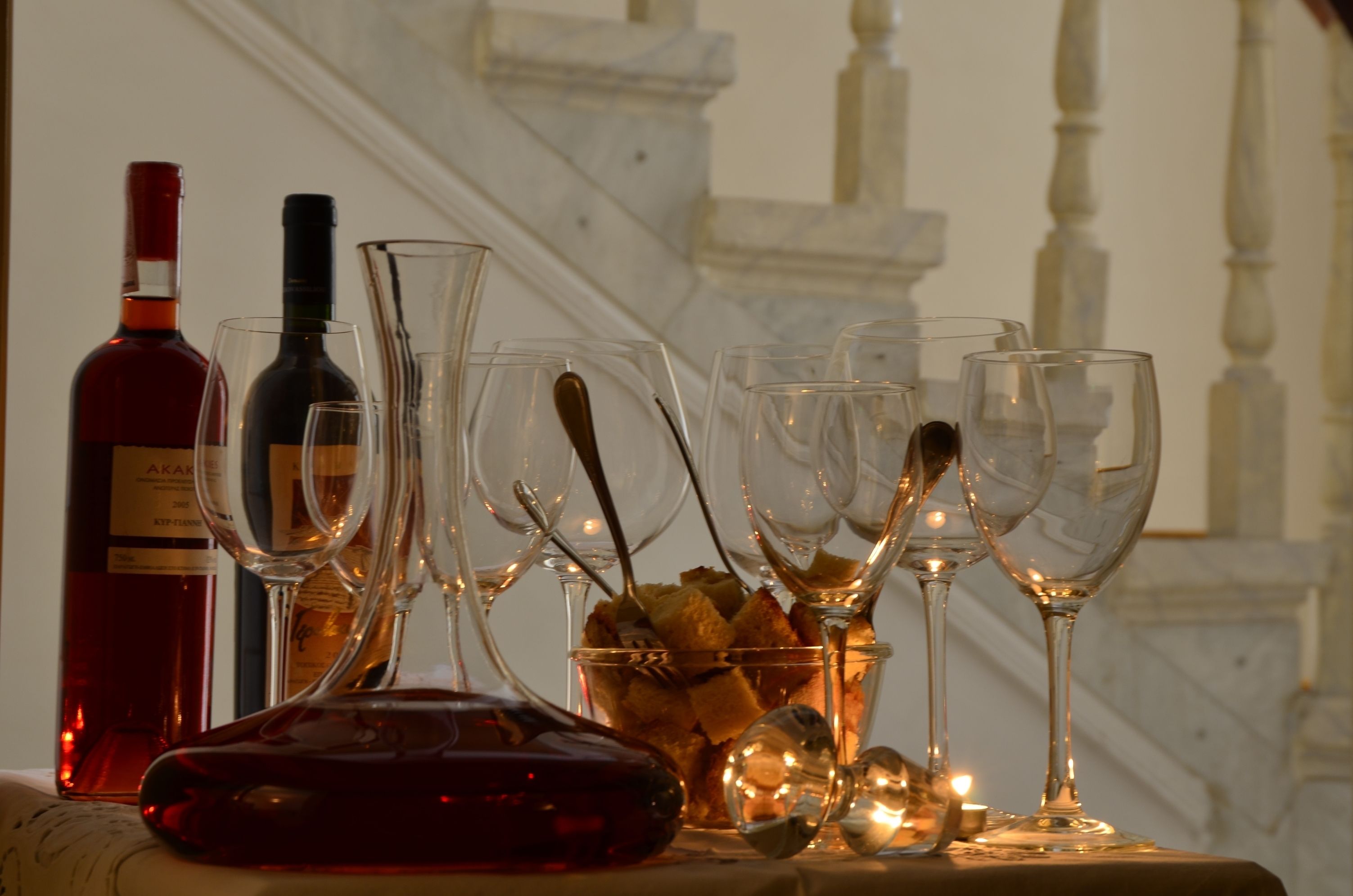 A table with wine bottles and glasses, a bowl of bread, and a candle.