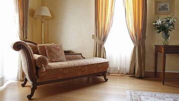 A vintage sofa with floral upholstery in a room with wooden flooring, a standing lamp, and a vase with flowers on a side table.