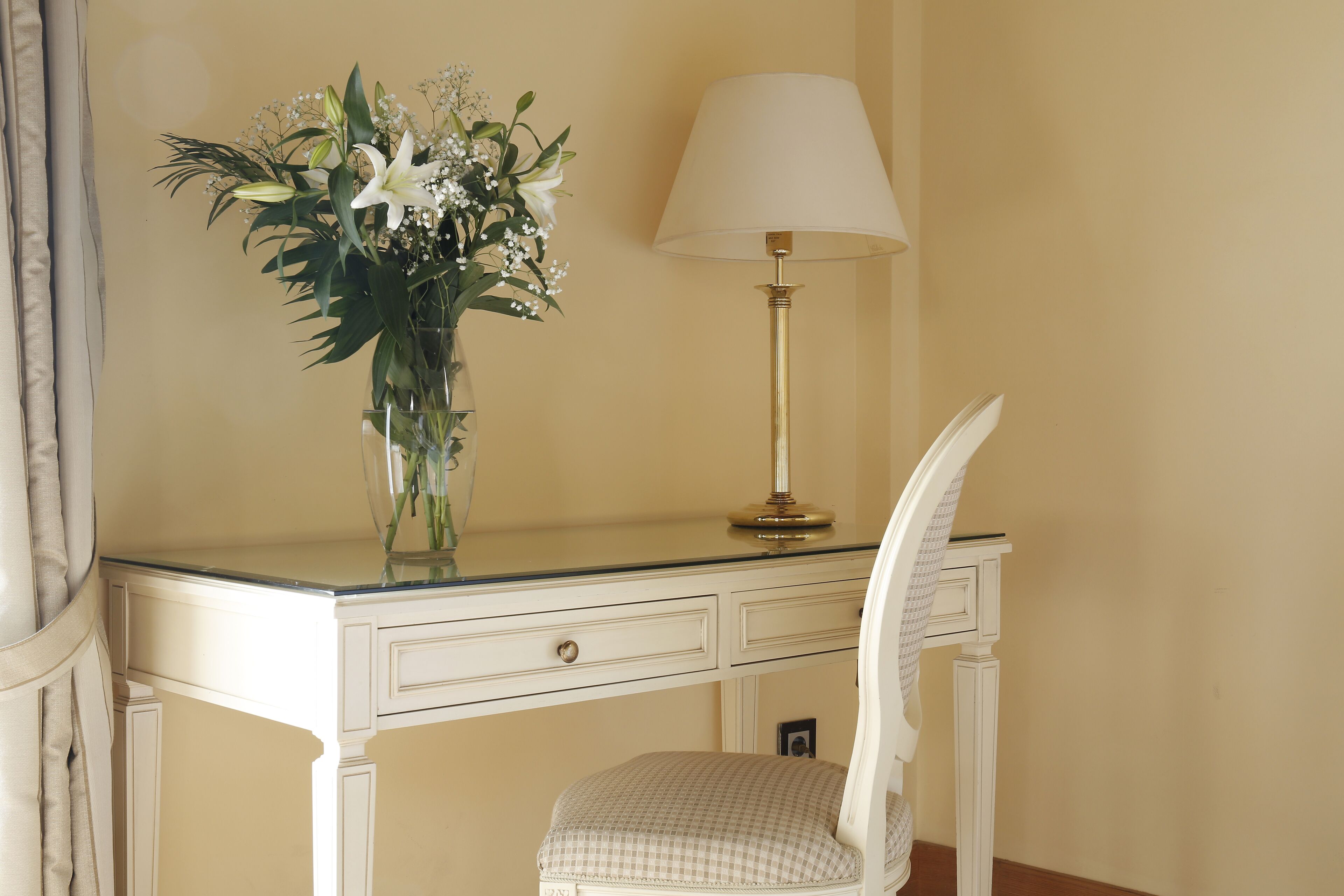 Un bureau blanc avec une lampe et un vase de fleurs.