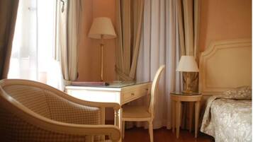 Une chambre d’hôtel avec un lit, un bureau et une chaise, une lampe et une fenêtre avec des rideaux.